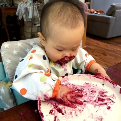 a picture of baby's hands and face covered in beet hummus