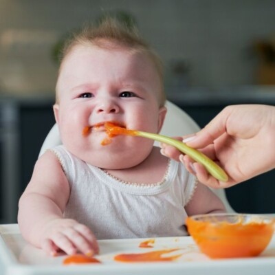 baby in high chair refusing to open mouth to mom holding a spoon with puree