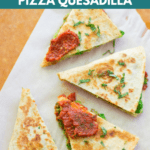 four pizza quesadilla triangles spread out on a parchment paper with pizza sauce spread on two pieces and fresh basil sprinkled throughout