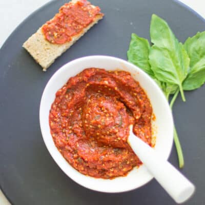 baby-friendly pizza sauce in a white bowl with a spoon and above it a toast spread with sauce and fresh basil on the side