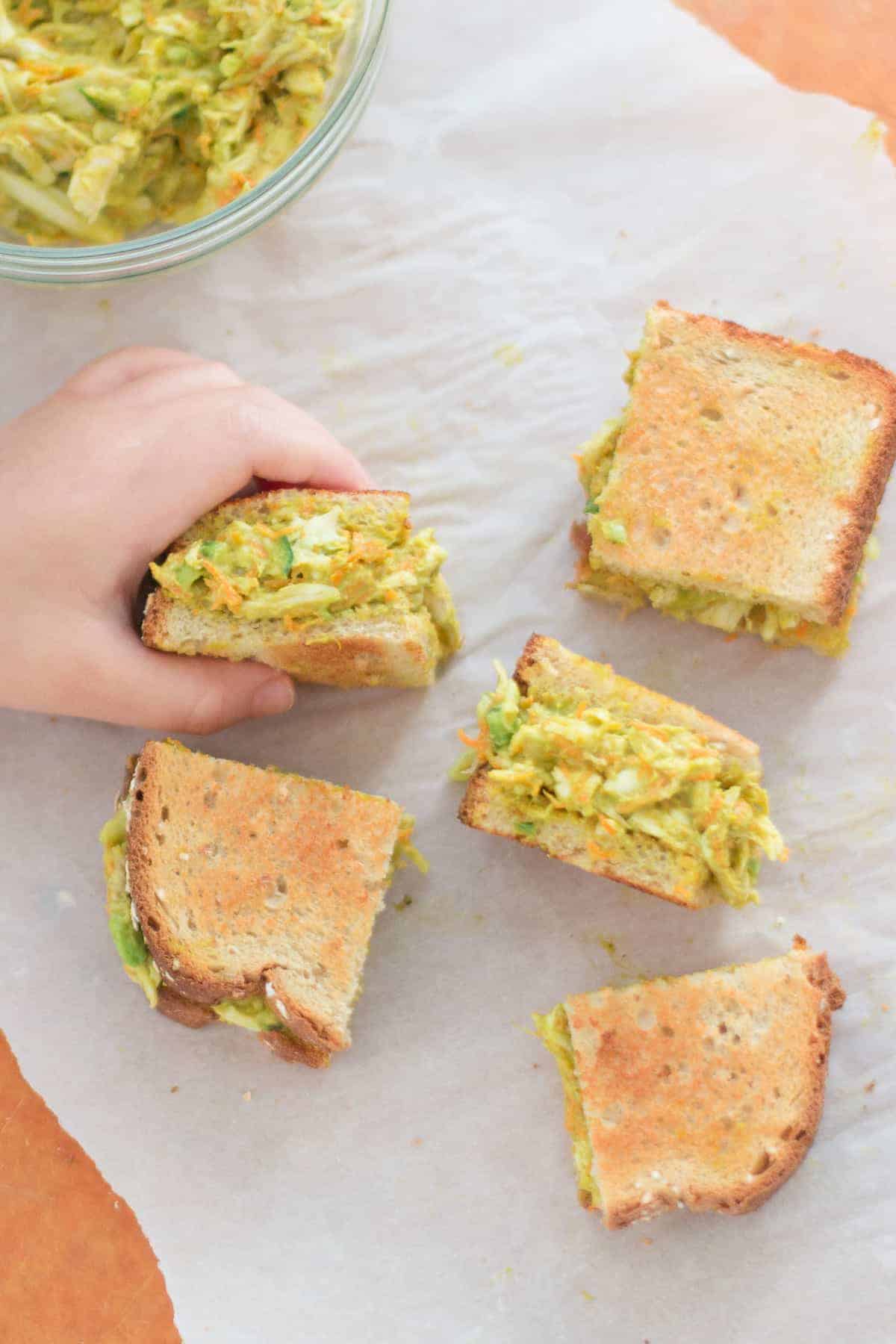 curry chicken avocado salad sliced into 5 small pieces with toddler's hand grabbing one