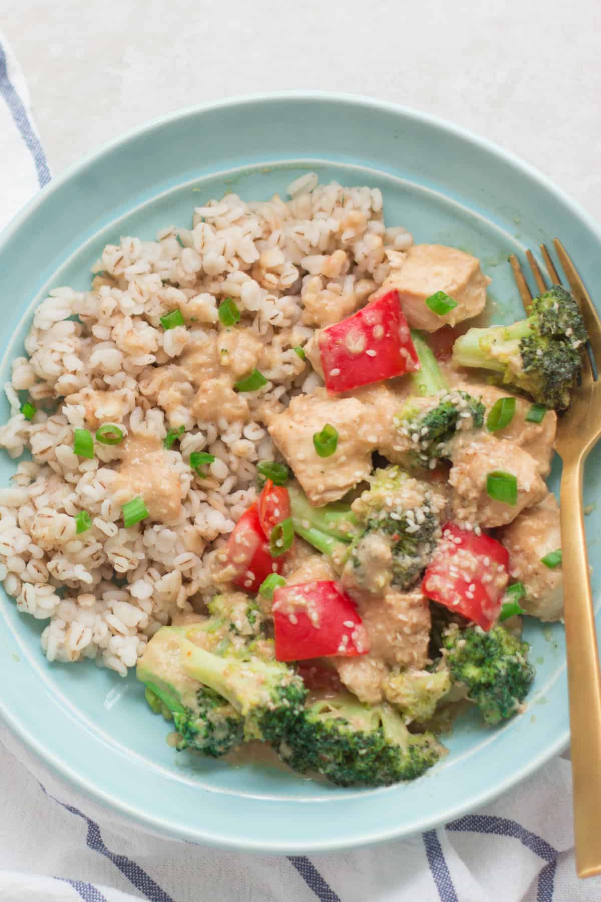 peanut chicken and broccoli served with barley on a blue plate with a a fork