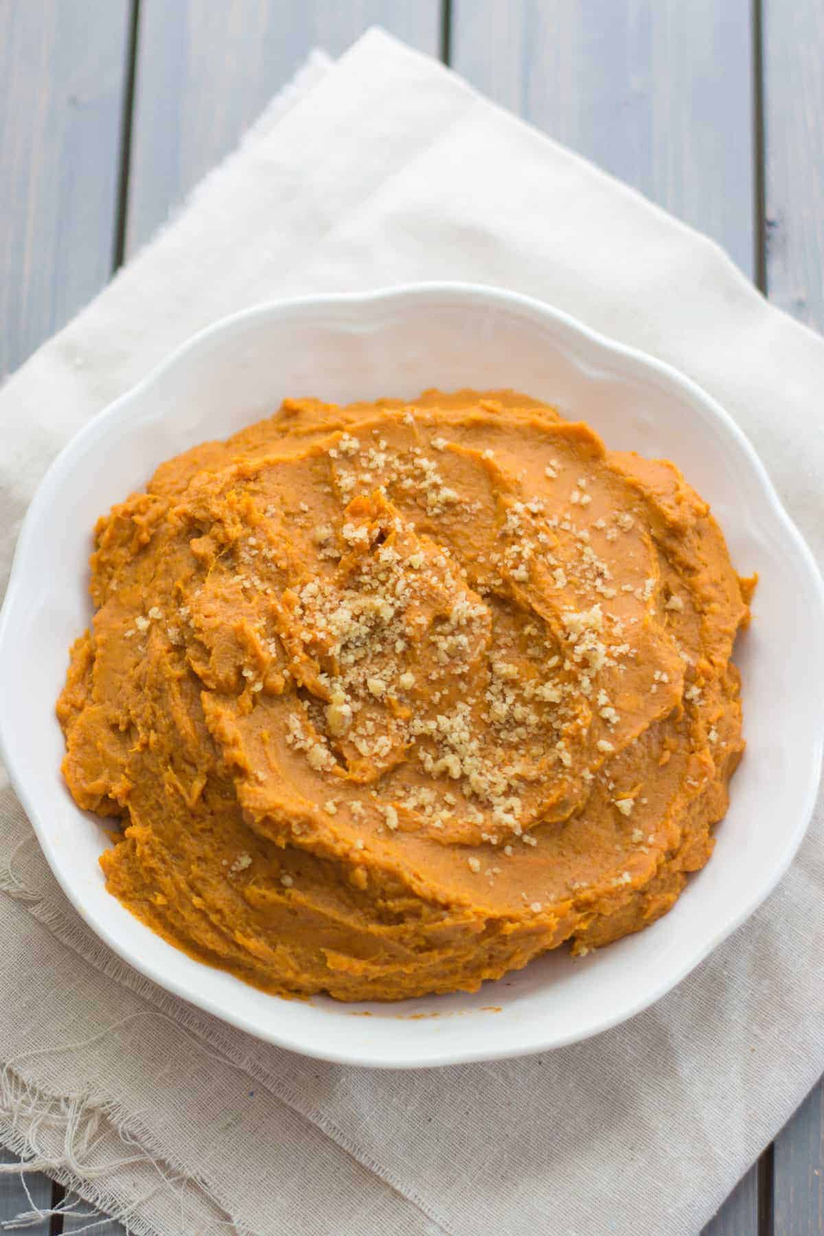 mashed sweet potatoes served in a white bowl and topped with ground walnuts