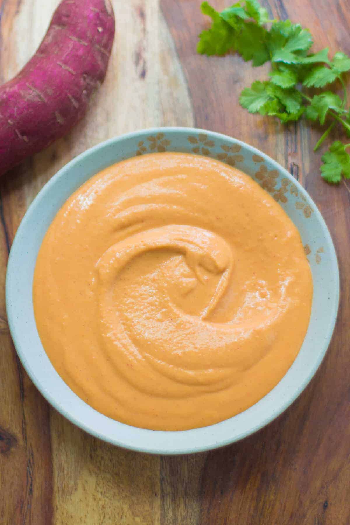 sweet potato sauce poured into a bowl with sweet potatoes and cilantro in the background