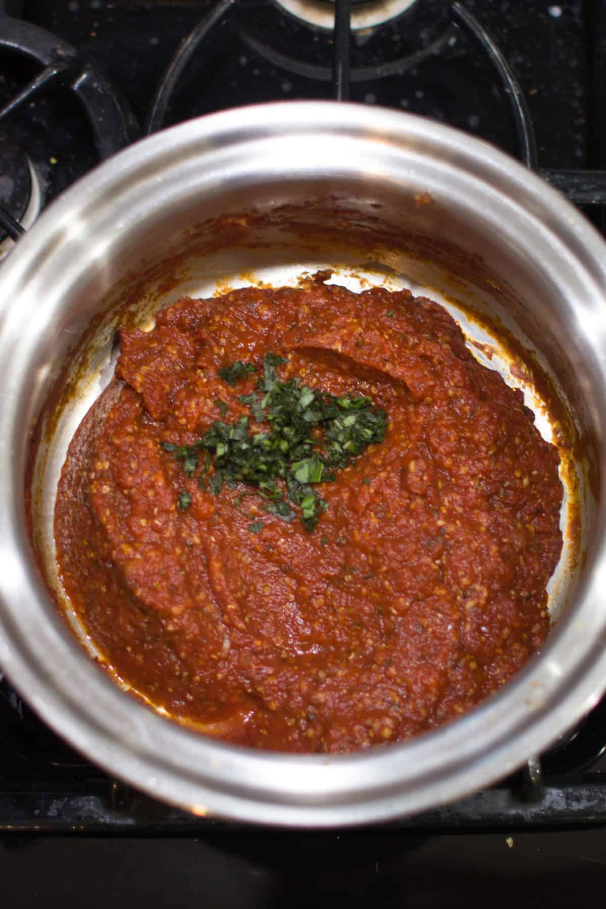 Finished pizza sauce in a stainless pan with basil.