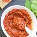 Homemade pizza sauce in a white bowl with a spoon and toast with a smear of the sauce.