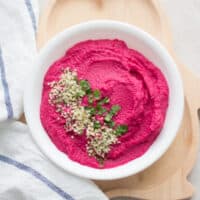 beet hummus in a white bowl with hemp seeds and cilantro sprinkled on the left side