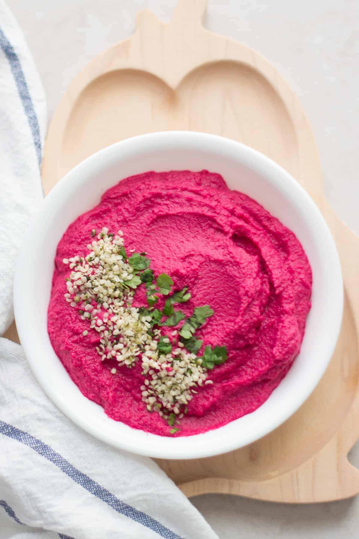 beet hummus in a white bowl with hemp seeds and cilantro sprinkled on the left side