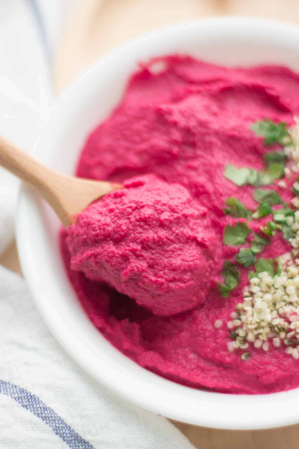 a close up shot of beet hummus on a wooden spoon
