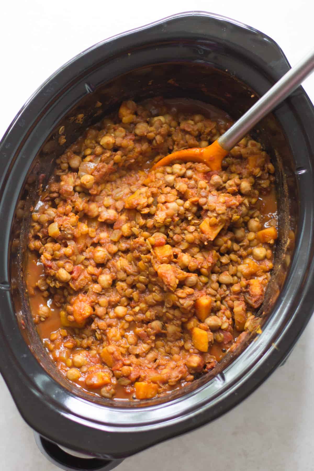 chickpea lentil chili in a slow cooker with an orange spatula