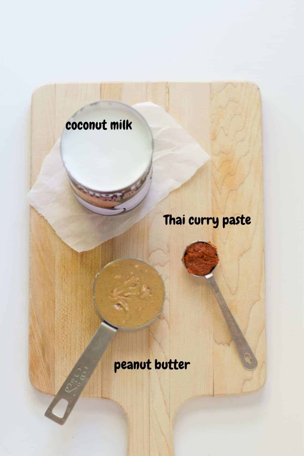 coconut milk, curry paste, and peanut butter laid out on a wooden board