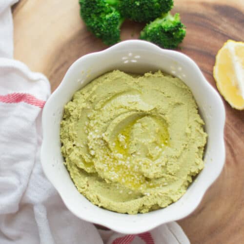 close up shot of broccoli hummus in a white bowl with drizzle of oil.