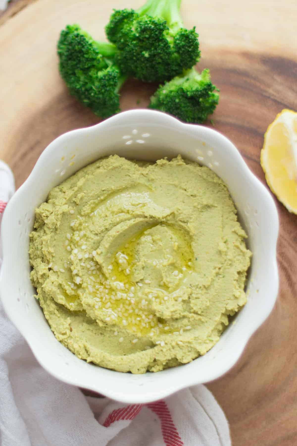 close up shot of broccoli hummus in a white bowl with drizzle of oil.
