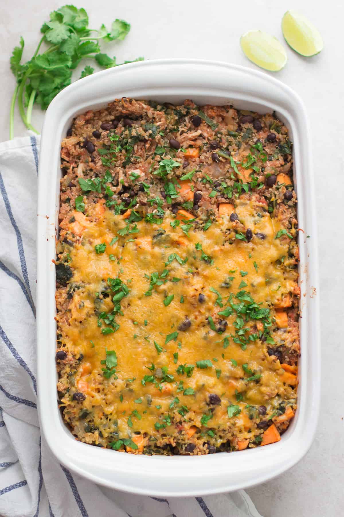 baked chicken spinach quinoa bake in a baking pan with chopped cilantro and lime.