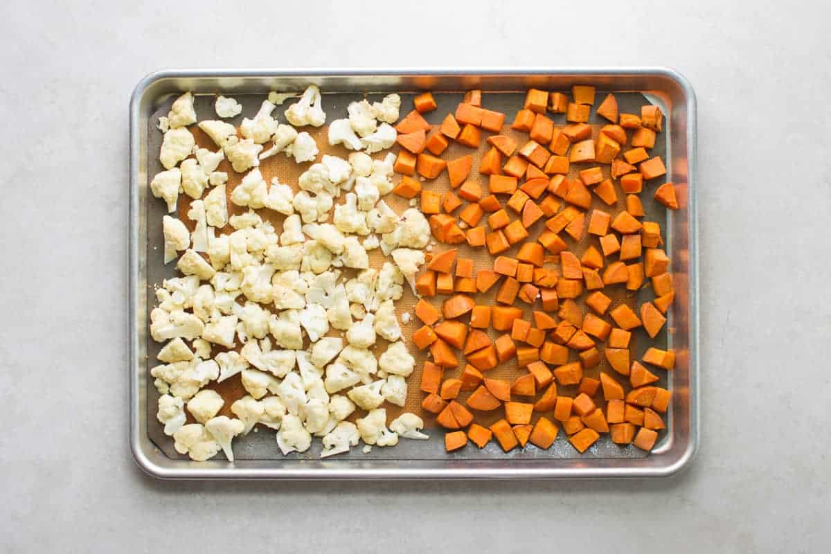 roasted bite-sized cauliflower and sweet potatoes on a baking sheet.
