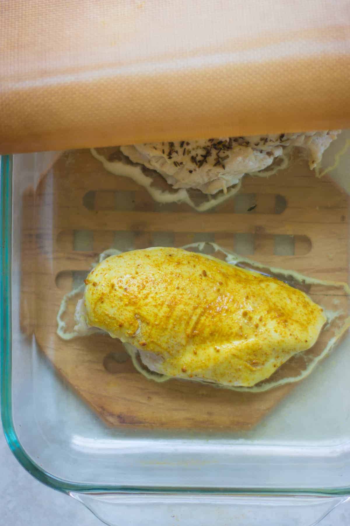 a piece of chicken breast seasoned with curry powder and baked, covered, in a glass oven-safe dish.