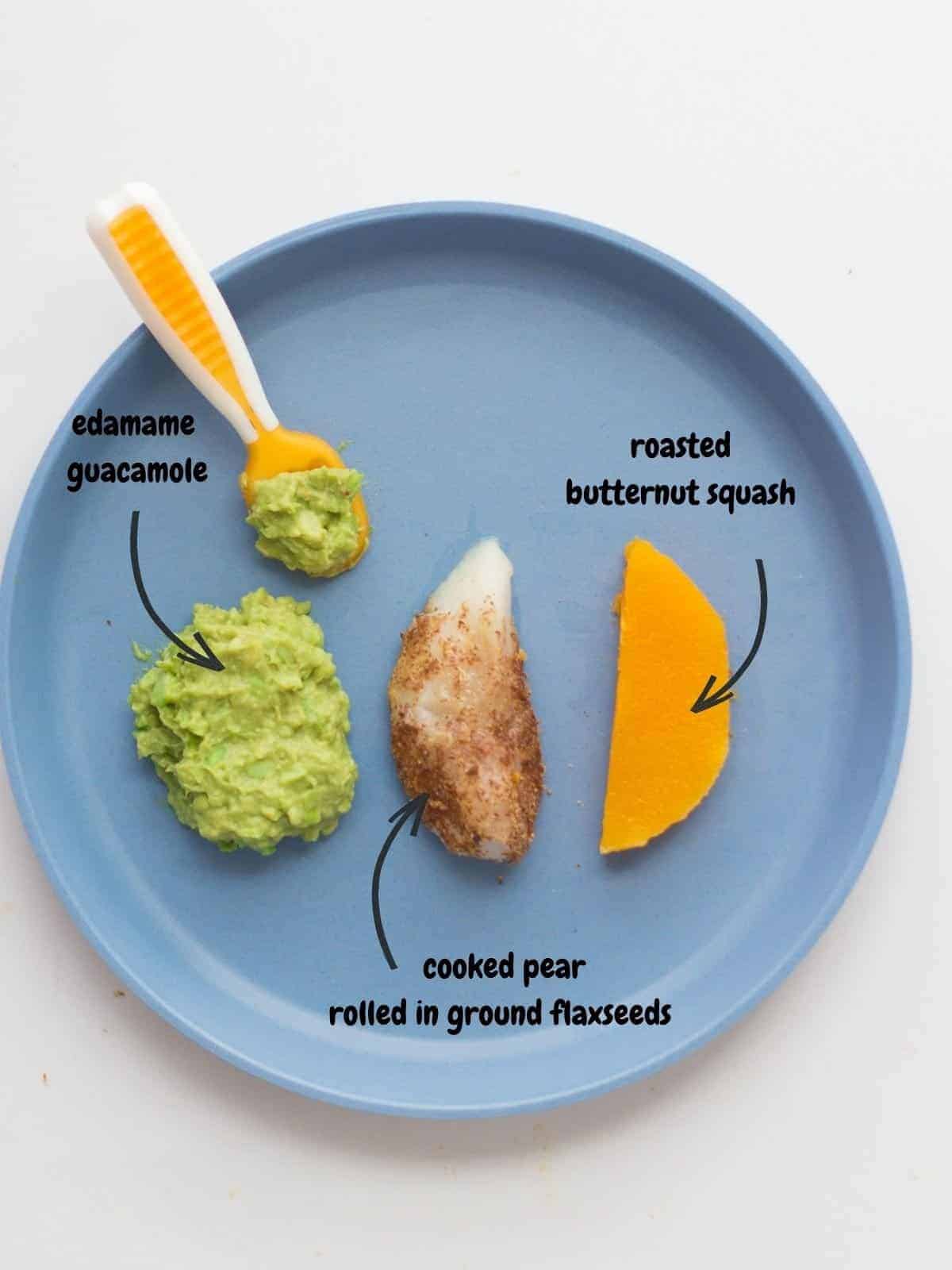 a baby's plate with a thick wedge of cooked pear rolled in flaxseeds, roasted butternut squash, and edamame guacamole.
