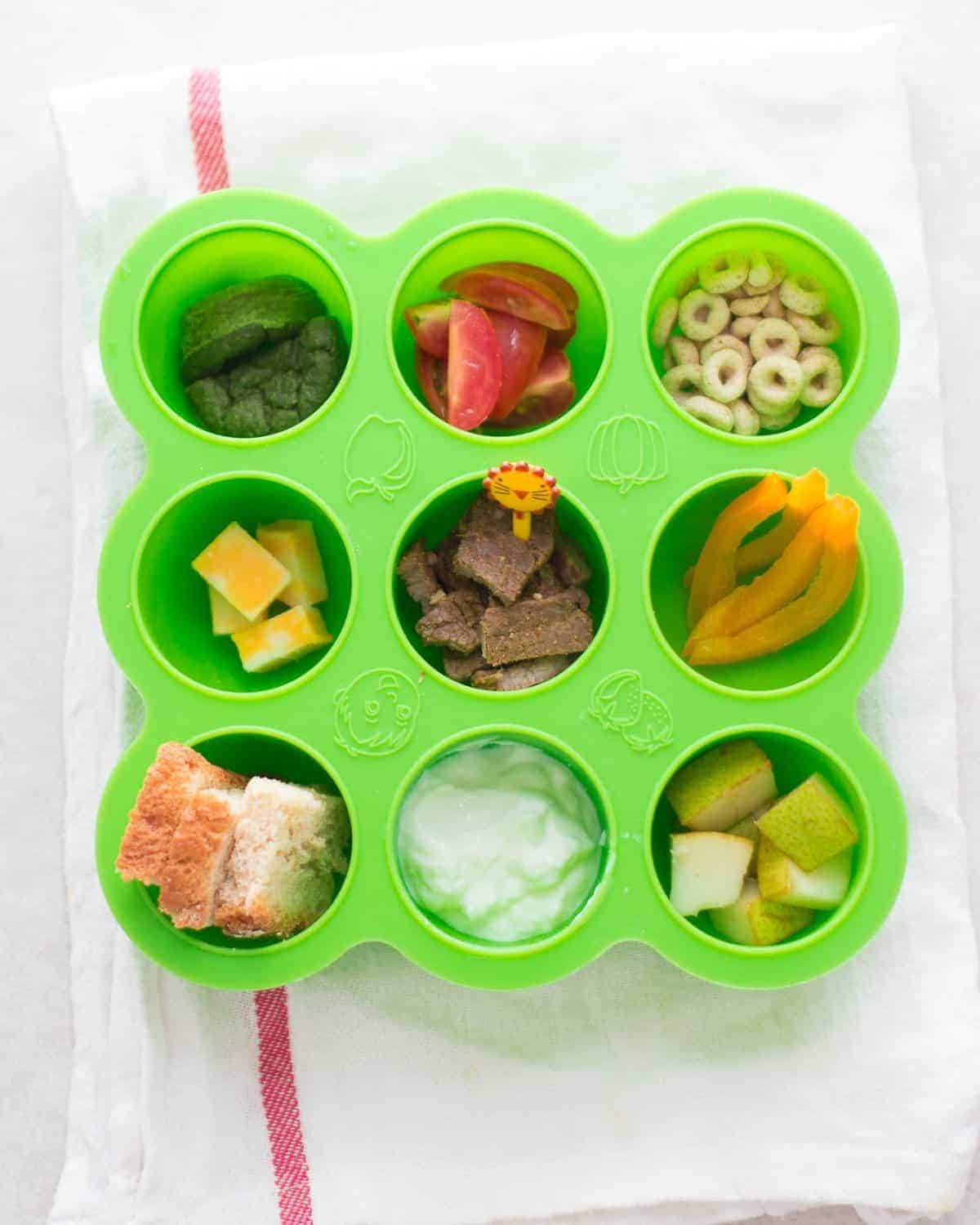 a snack tray with an assortment of finger friendly foods, like cereal, cheese, bell peppers, and cubed beef.