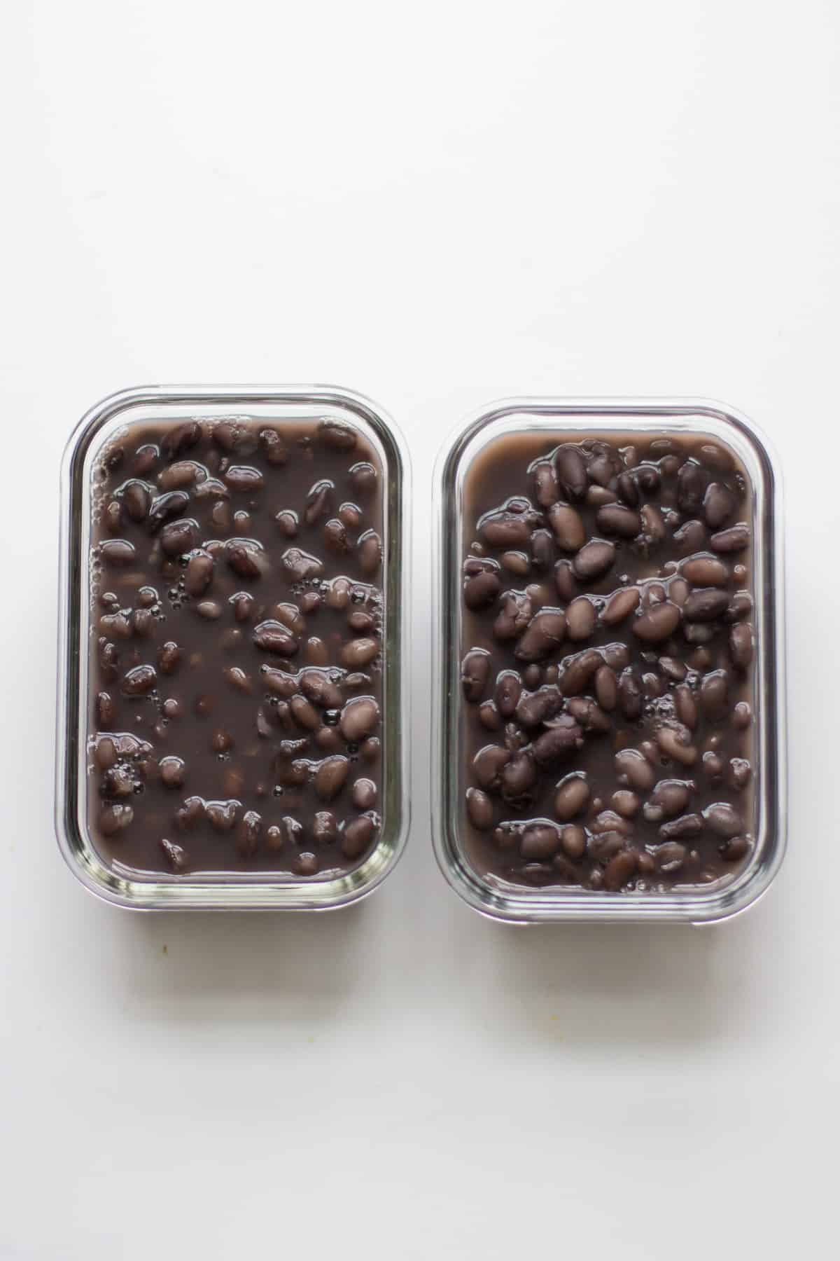 Two glass containers with black beans and cooking liquid.