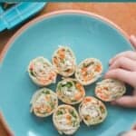 8 tortilla roll ups placed on a blue plate with toddler's hand grabbing one.
