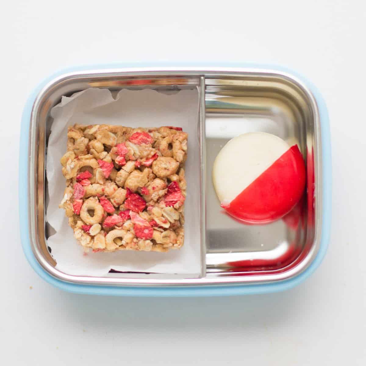 one square piece of cereal bar with babybel cheese in a stainless steel snack container.
