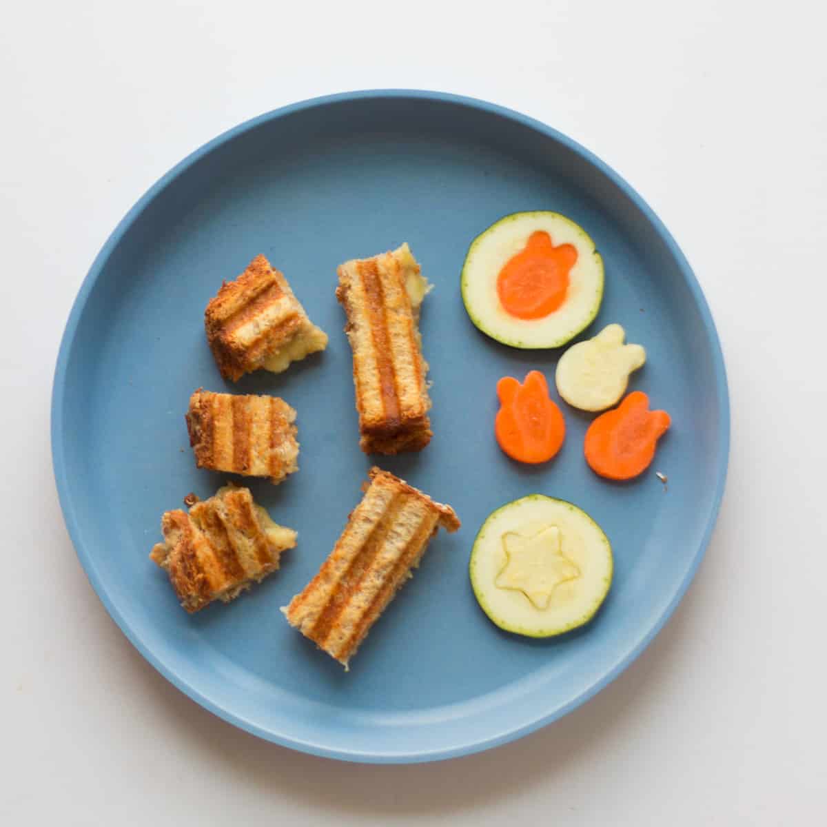 Hummus grilled cheese cut into cubes and strips with zucchini and carrots cut into rabbit and star shapes.