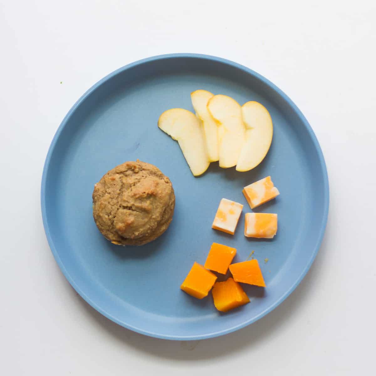 A whole muffin, apple slices, cubed cheese, and butternut squash.