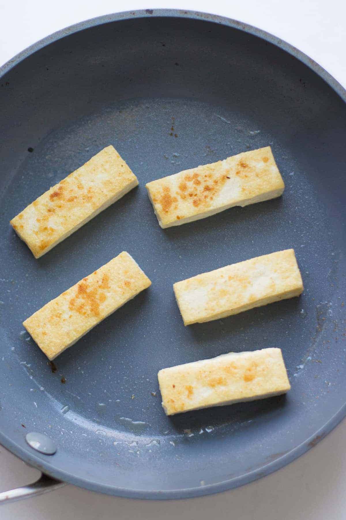 five tofu strips fried on a pan.