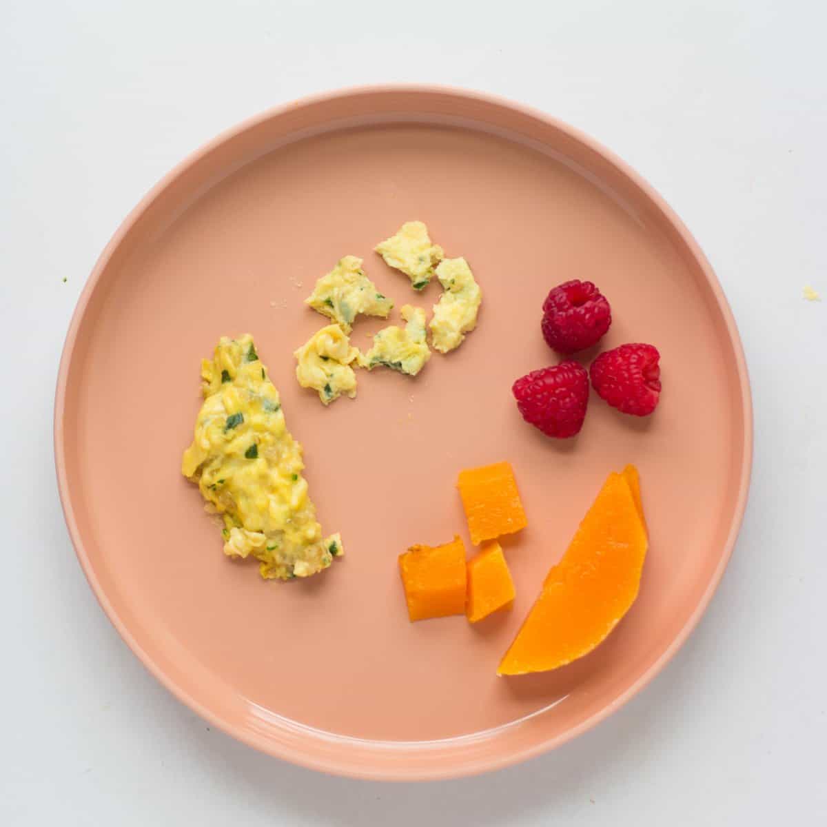 a baby's plate with eggs served two ways as a strip and bite sized pieces, butternut squash served two ways, and raspberries.