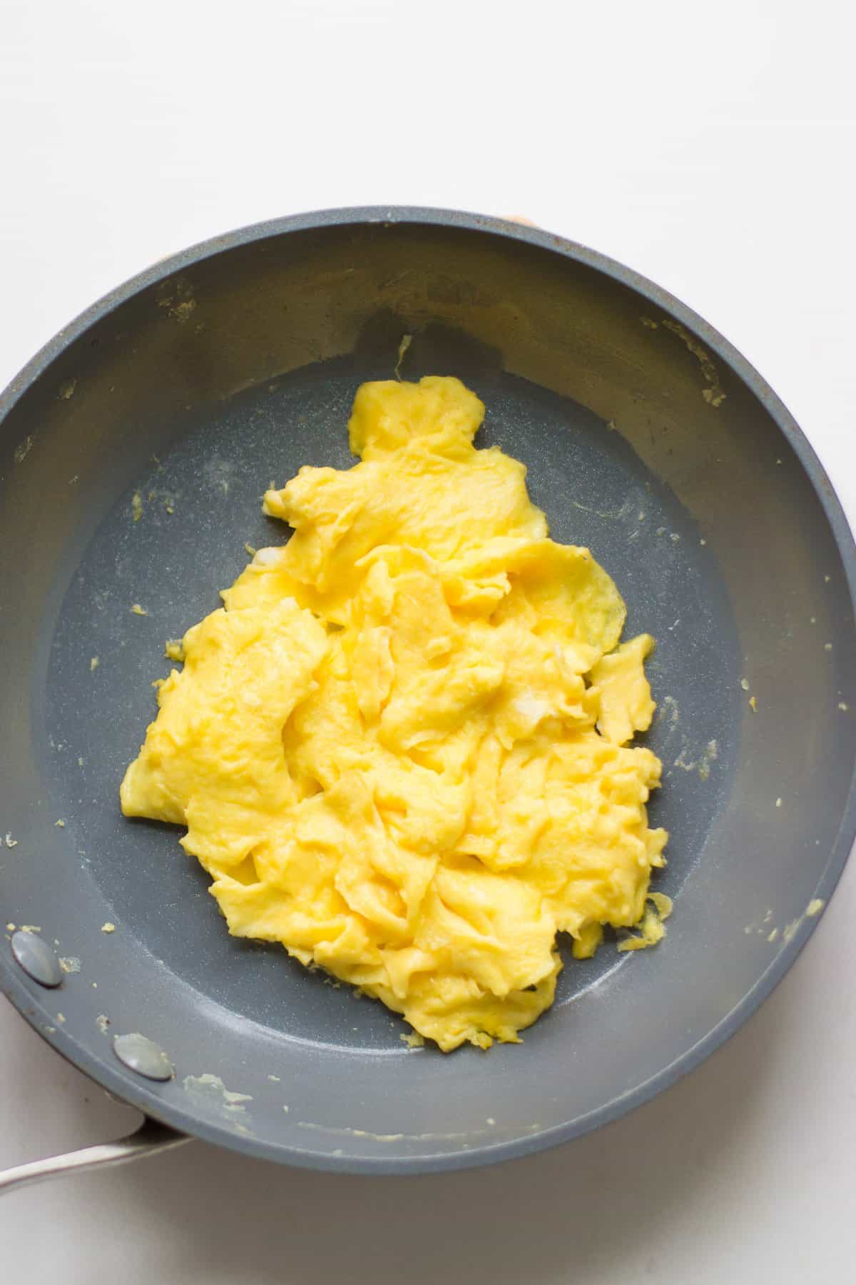 cooked scrambled eggs with large curds in a nonstick pan.