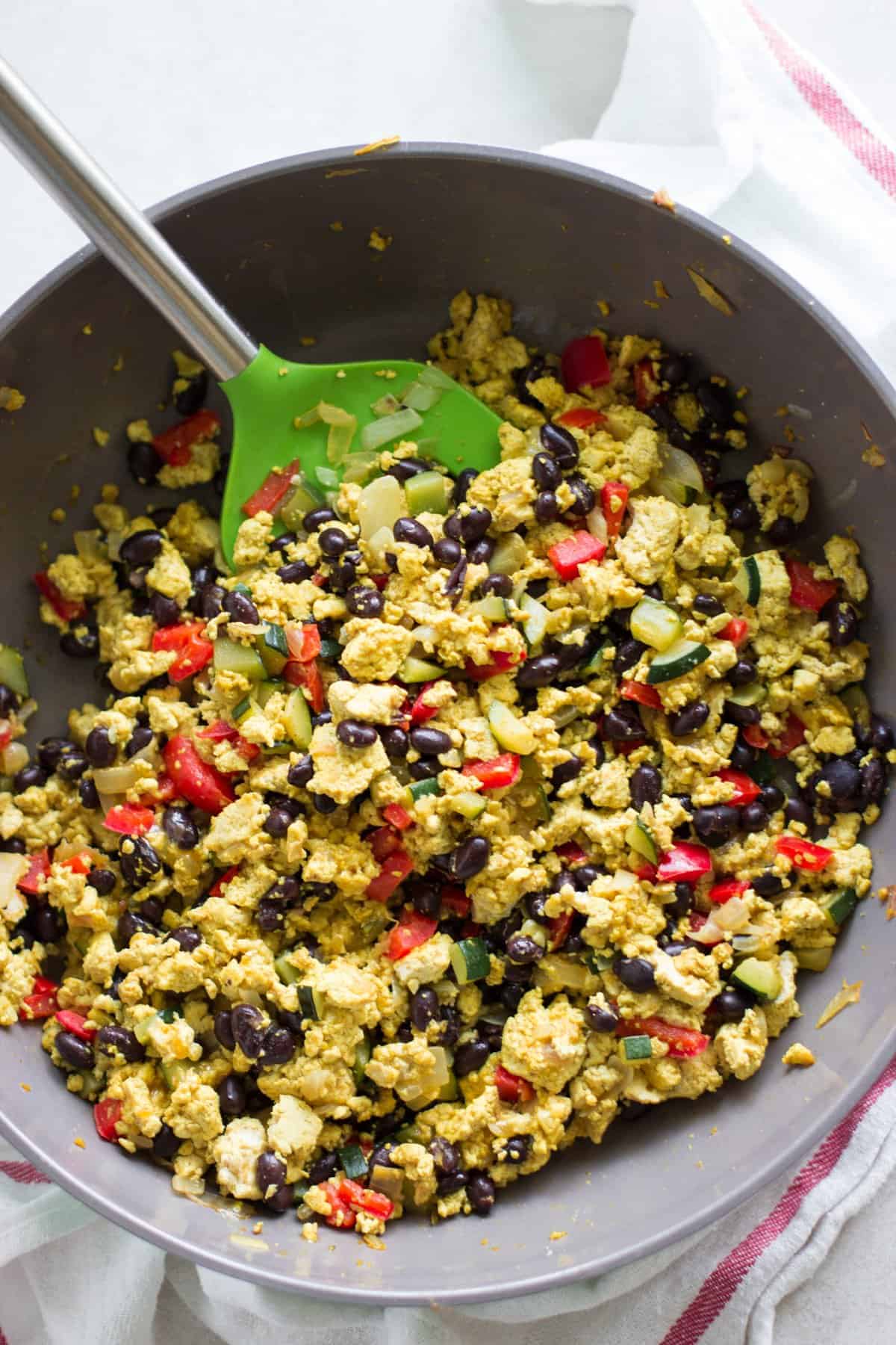 scrambled tofu with vegetables and beans in a large pan with a green spatula.