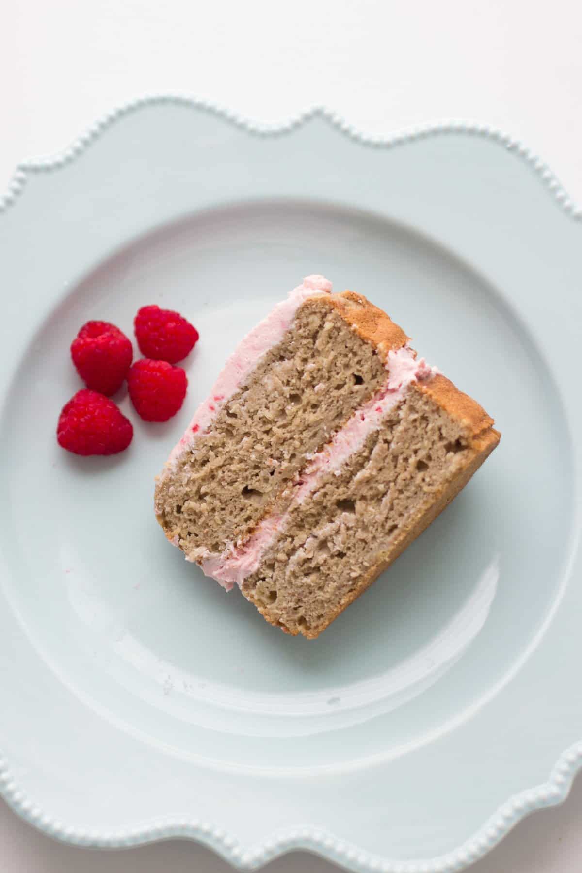 a sliced piece of cake on a blue plate with fresh raspberries on the side.