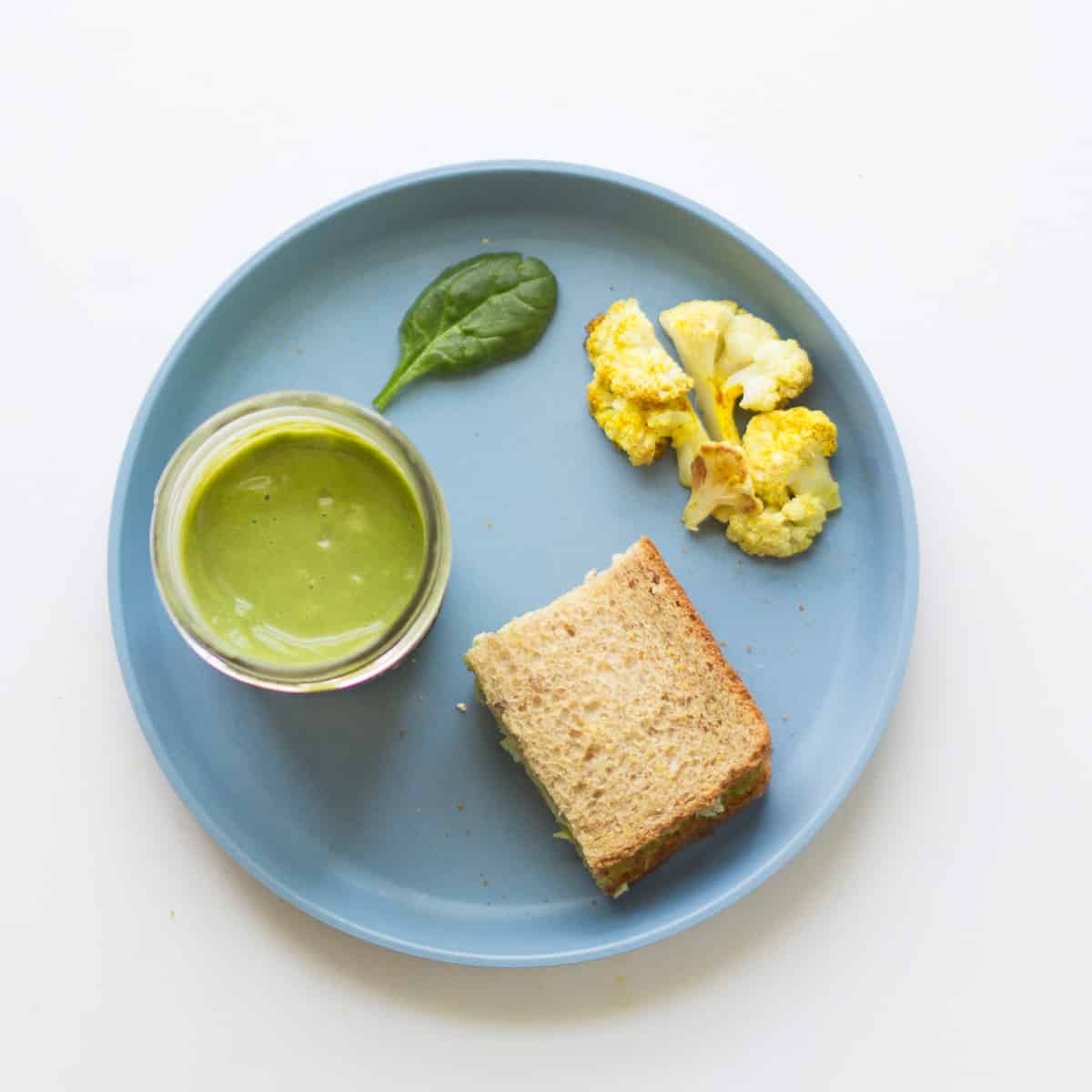 Green smoothie with a sandwich half, curried cauliflower, and one spinach leaf.