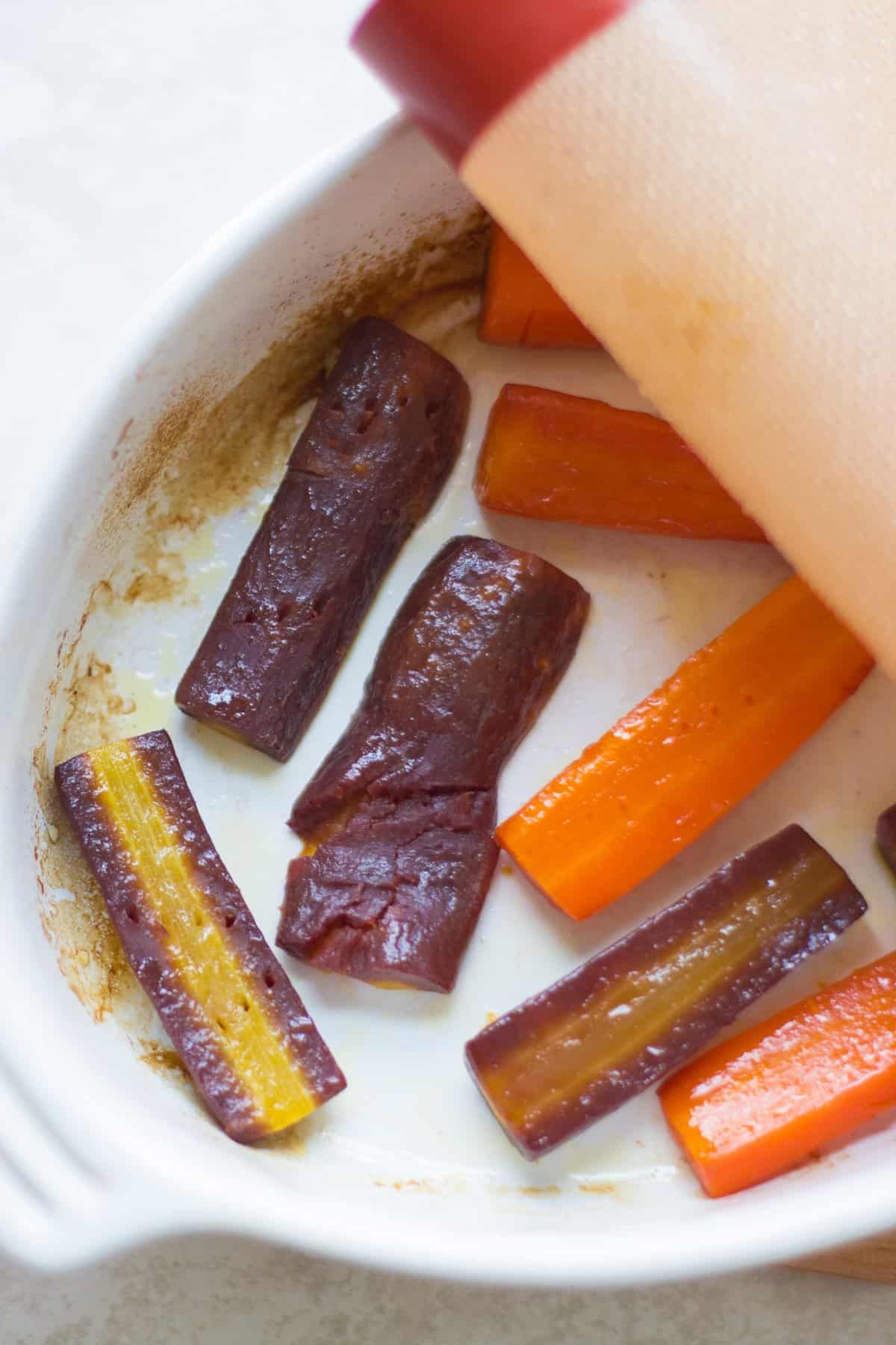 steam roasted purple and orange carrots in a white baking pan.
