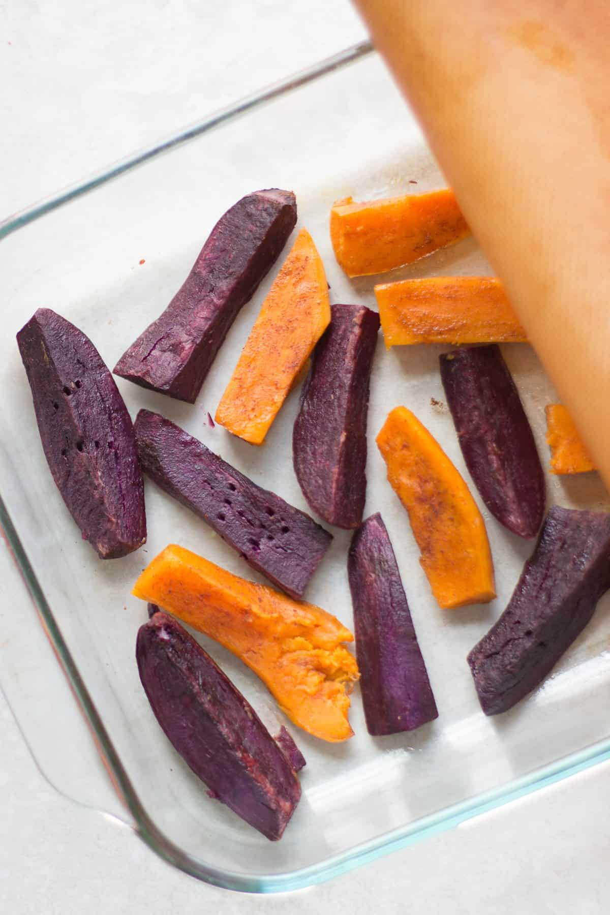 Purple and orange sweet potatoes steam roasted in a glass pan.
