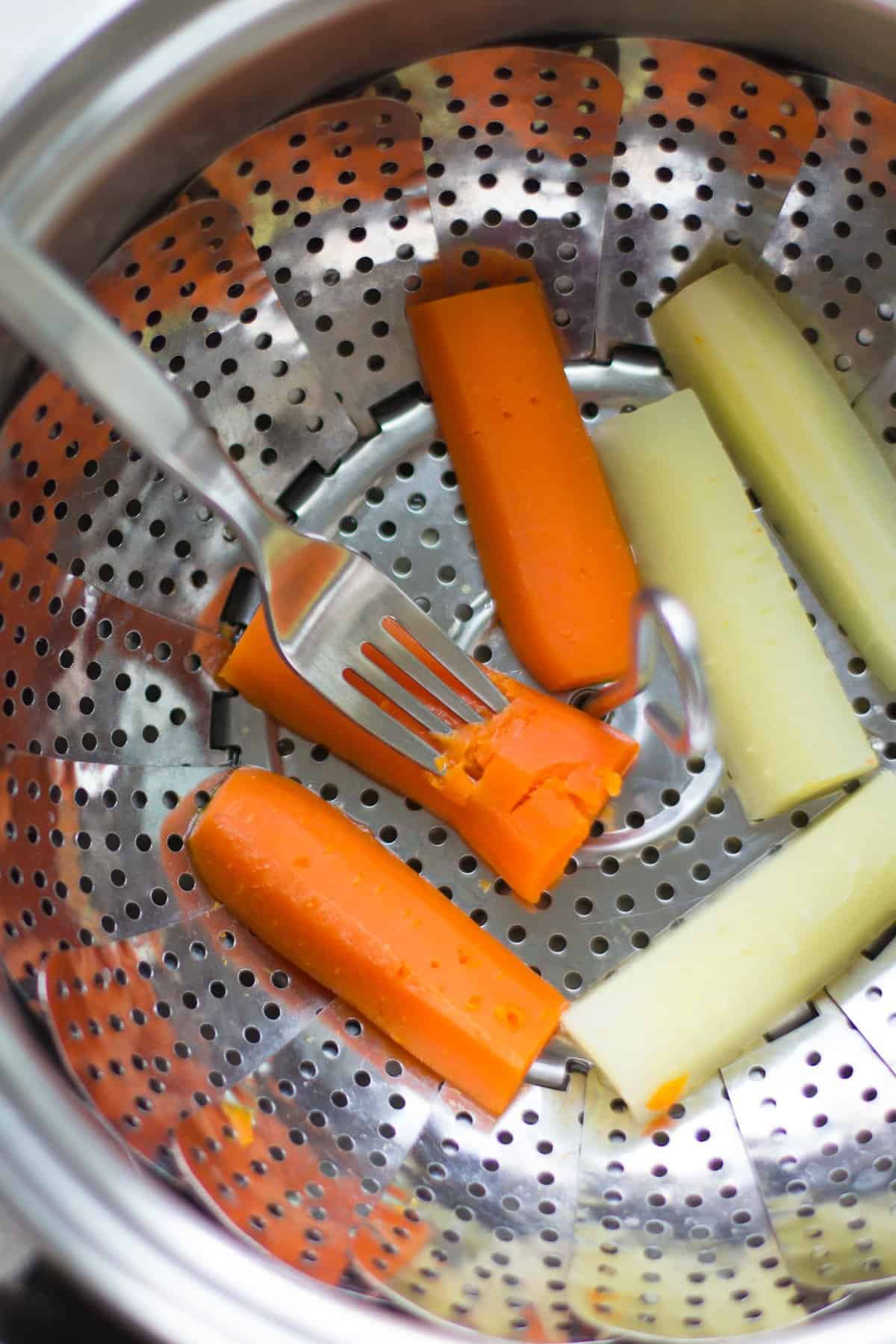 Steamed white and orange carrots in a pot.