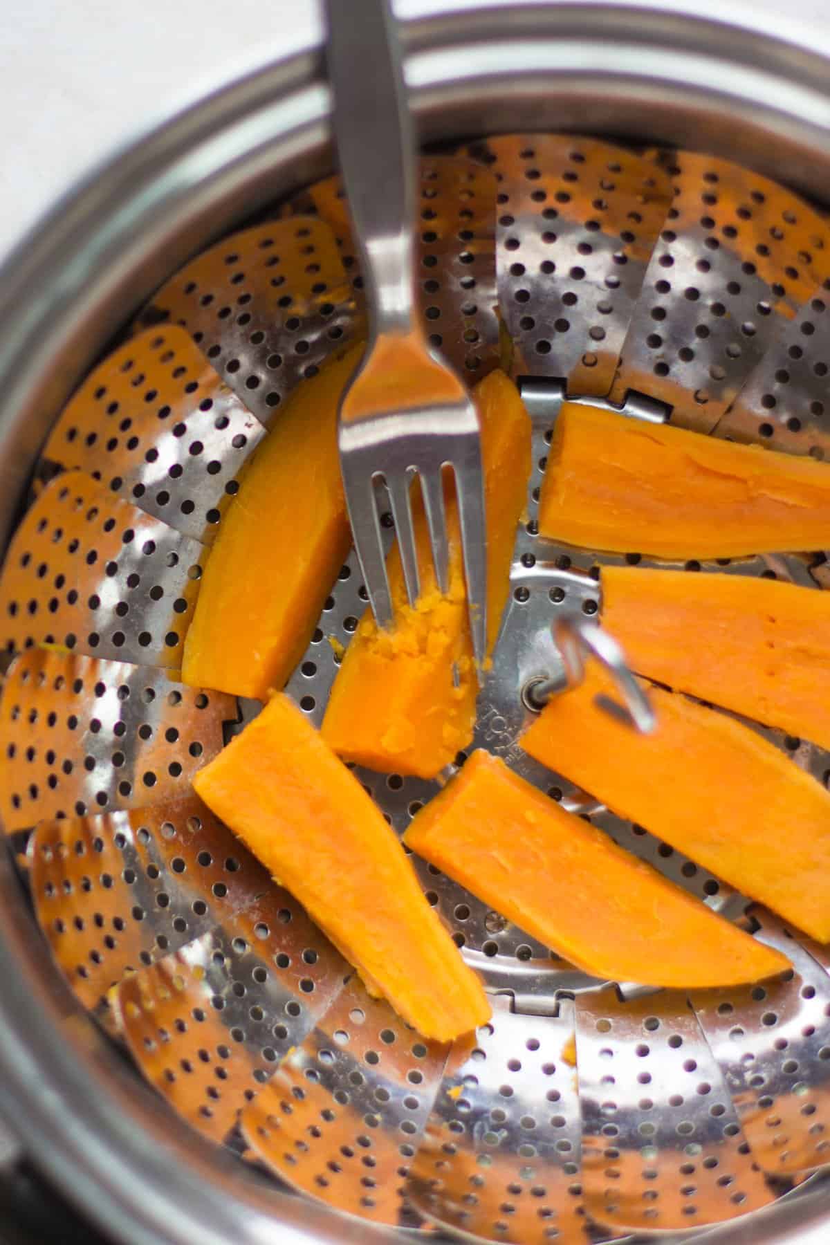 Steamed orange sweet potatoes with one piece pierced easily with a fork.