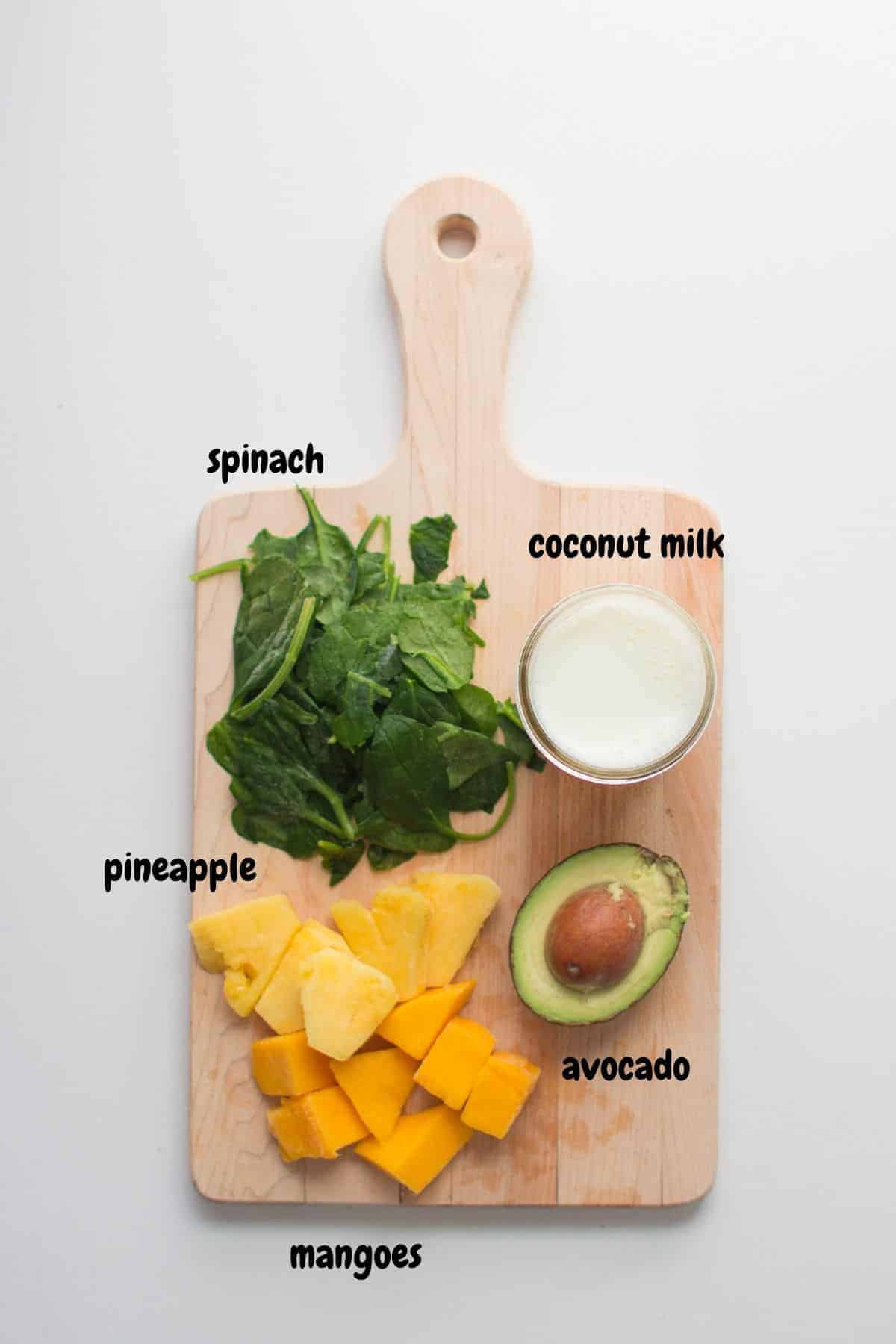 ingredients for the tropical green smoothie laid out on a wooden board.