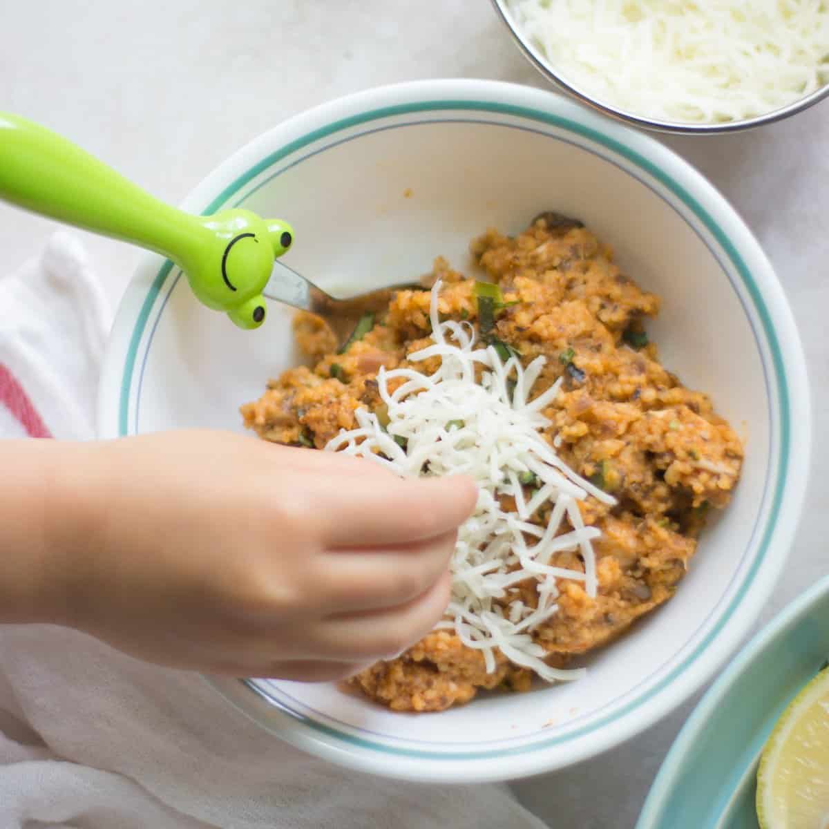 Quinoa casserole in a bowl with toddler adding cheese.