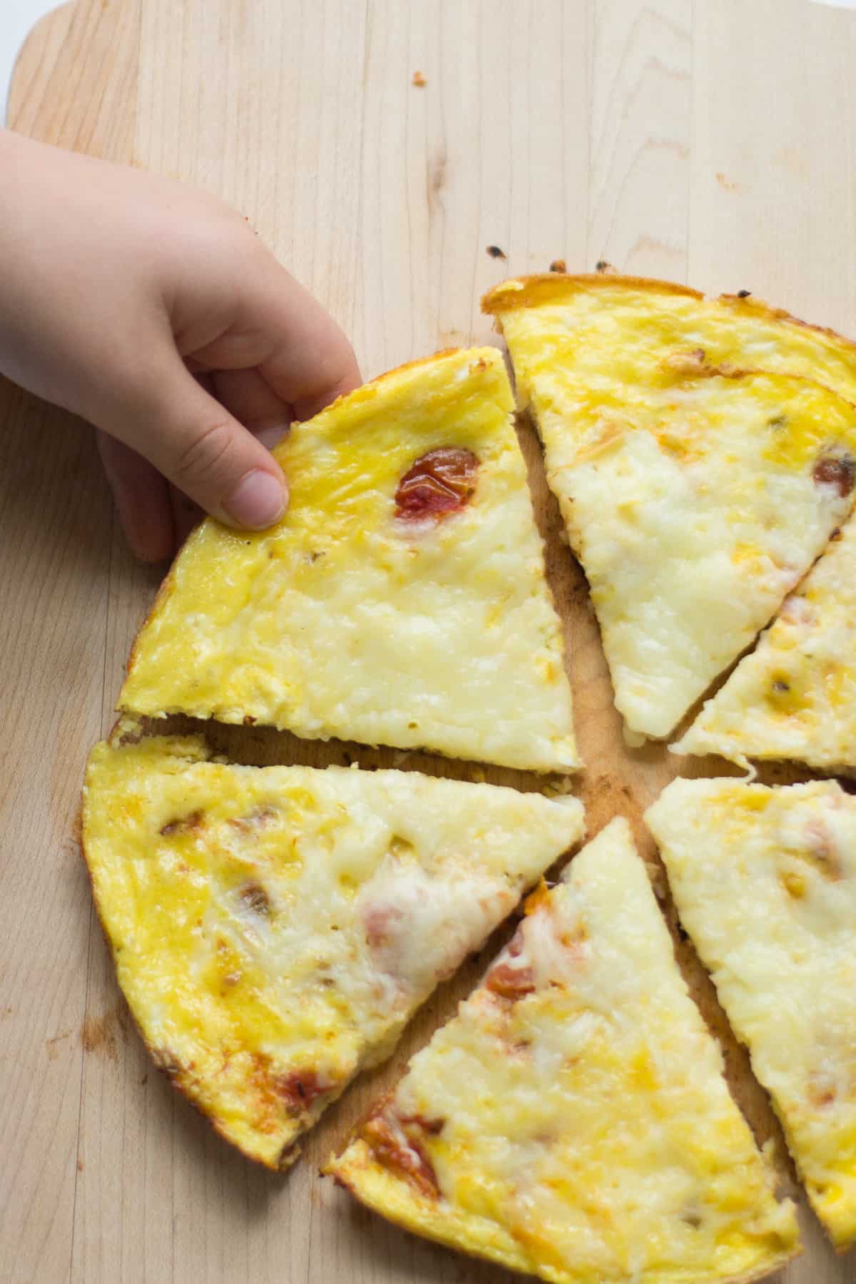 Toddler's hand grabbing a slice of pizza eggs.
