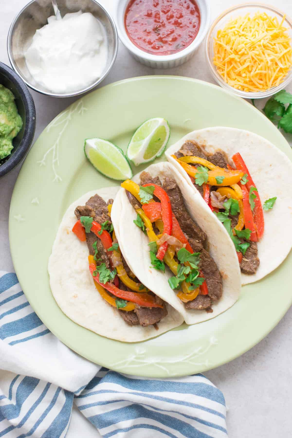 a close up shot of three steak fajita tacos with bell peppers, cilantro, and lime slices.