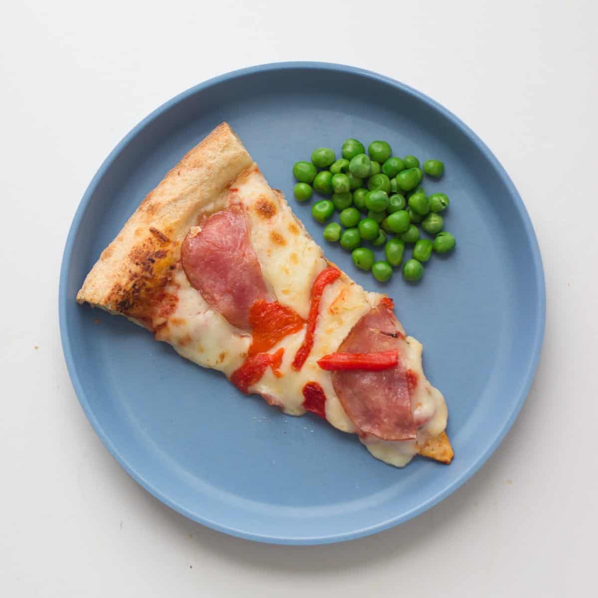 A slice of pizza with frozen peas.