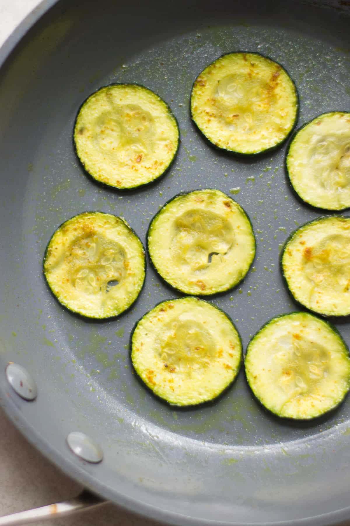 Sauteed zucchini rounds in a pan.