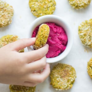 A toddler's hand dipping one of the nuggets in beet hummus.
