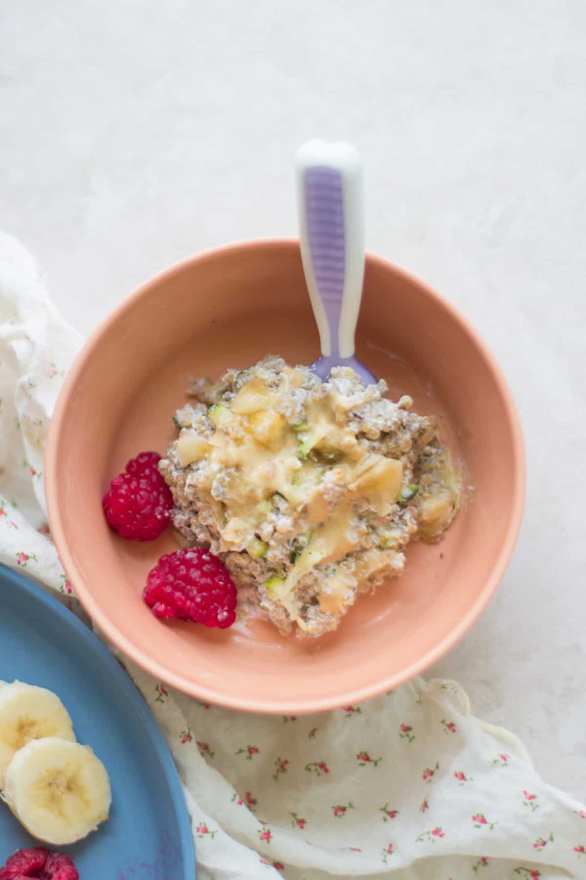 Quinoa bake served in a baby bowl with thinned out peanut butter and two raspberries.
