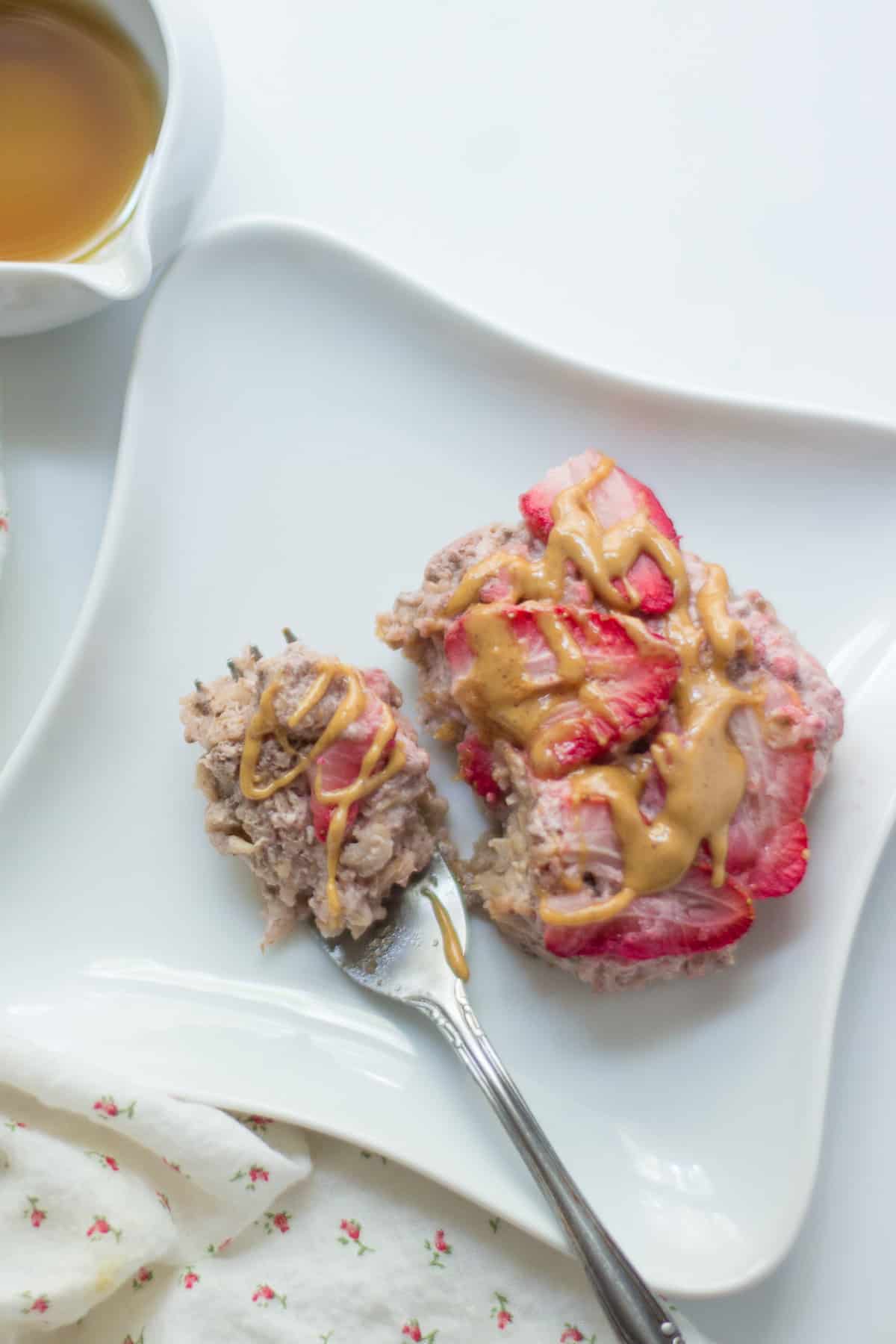 A slice of strawberry oatmeal on a plate with a drizzle of peanut butter and maple syrup.