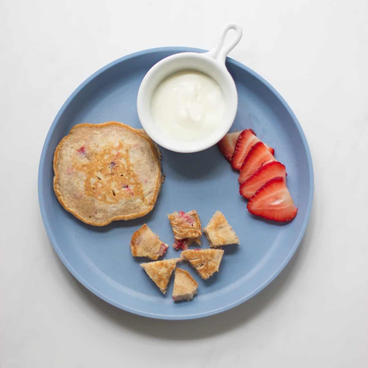 A toddler's breakfast plate with pancakes, yogurt, and fresh strawberries.