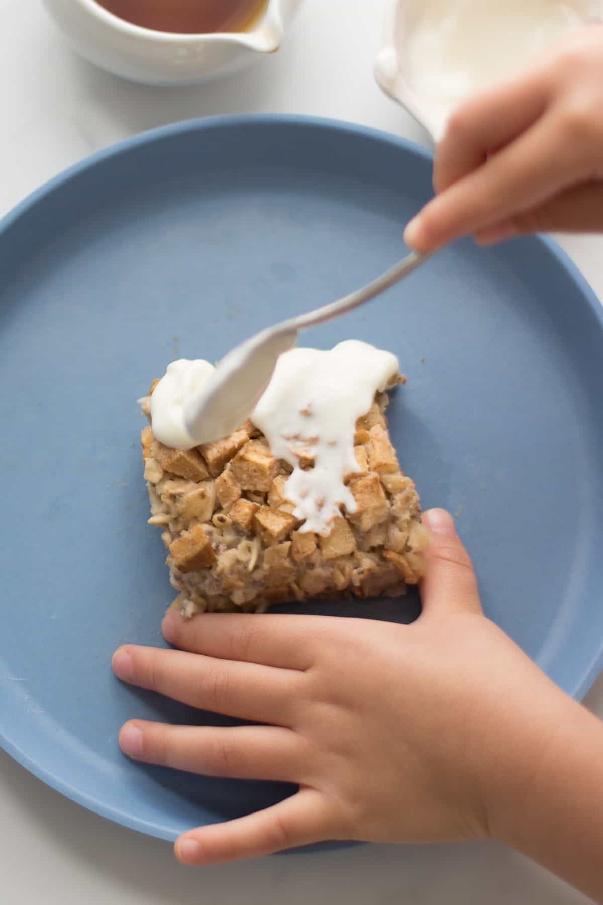 toddler spreading yogurt on top of oatmeal slice.