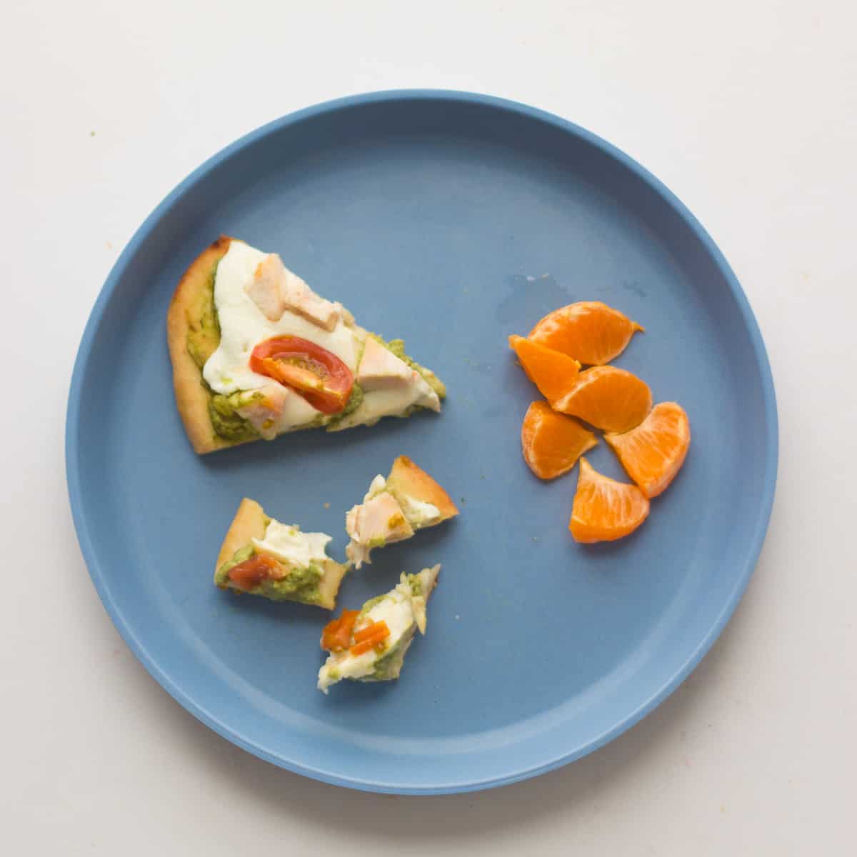 a small slice and bite sized pieces of pizza with diced oranges.