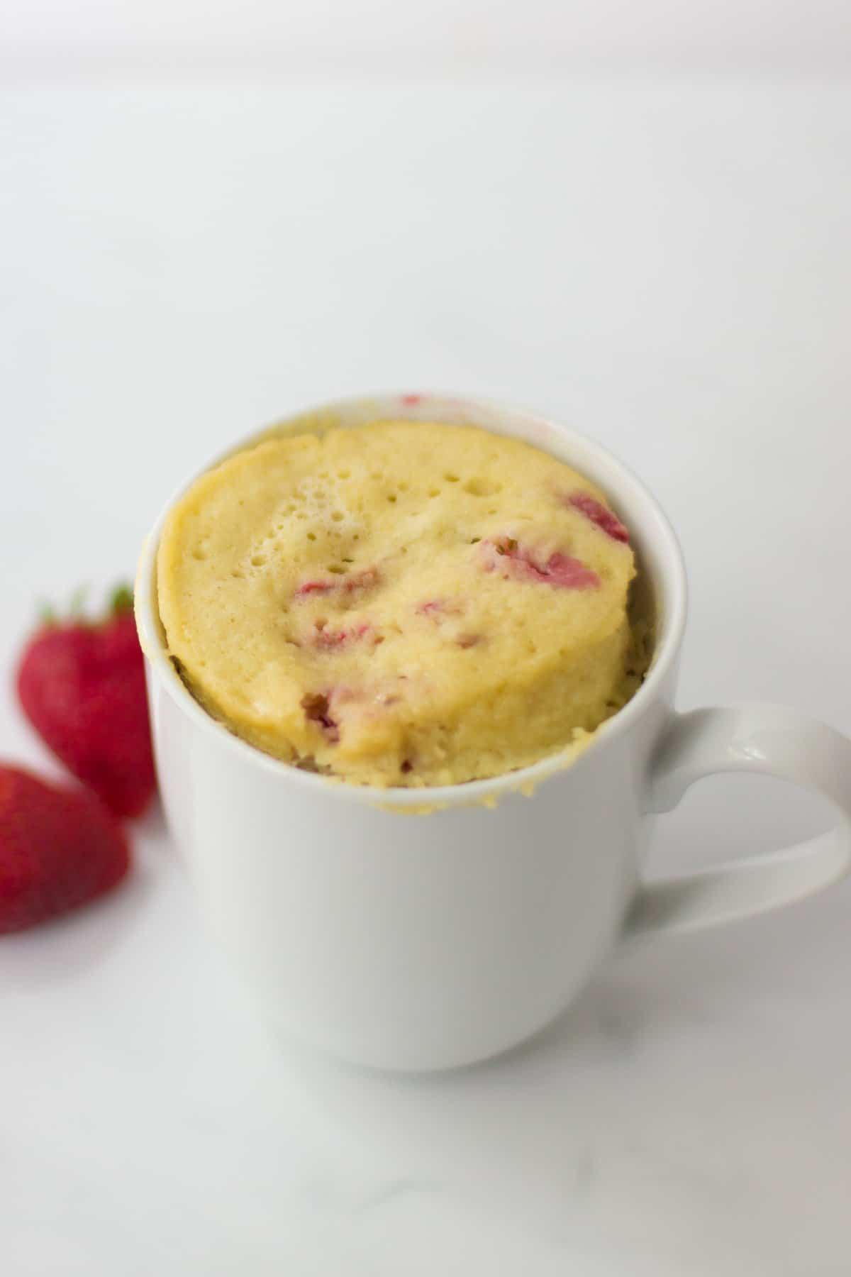 Microwaved mug cake with strawberries in the background.